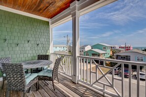 A covered porch with a table and chairs, a green brick wall, and a view of colorful houses in the background. - 2 Minutes to the Beach, Ocean Views, Side by Side Homes, Rent Separate/Together (Kure Beach)
