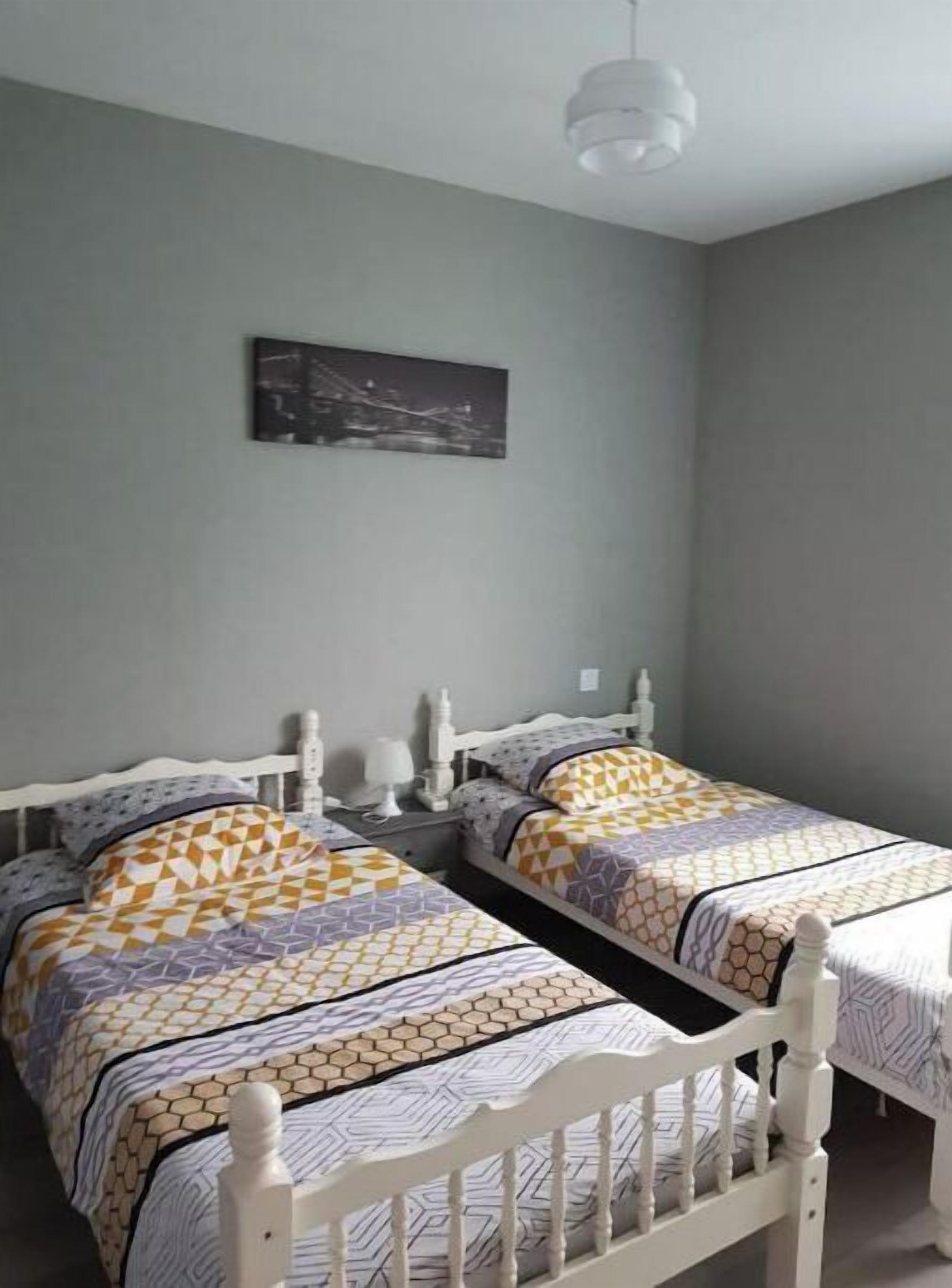 A bedroom with two beds, a nightstand, a lamp, and a ceiling light.