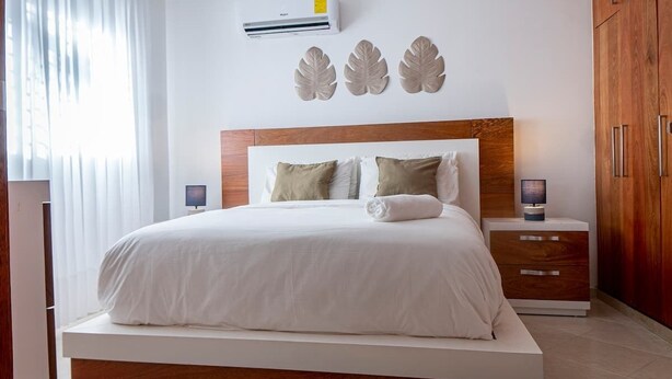 Une chambre à coucher moderne avec un grand lit, une tête de lit en bois et une table de chevet avec une lampe.
