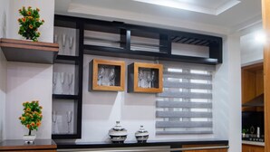 Une cuisine moderne avec un plan de travail noir, deux tabourets en bois et une fenêtre équipée de stores.