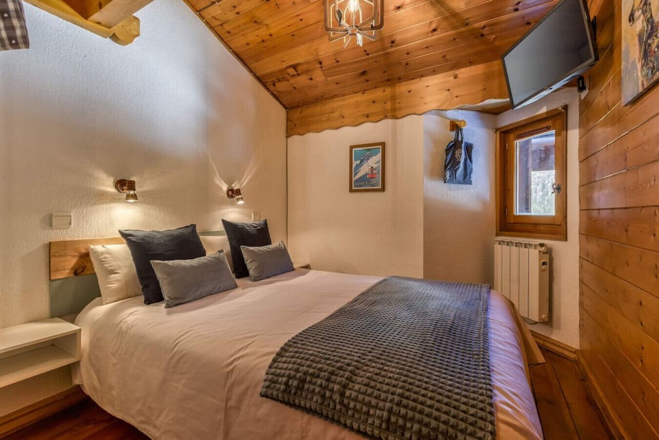 Une chambre avec un plafond en bois, un lit avec des oreillers, un téléviseur fixé au mur et une fenêtre.