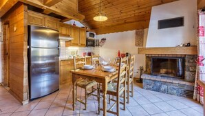 Una cocina de madera con una mesa de comedor para cuatro personas, una chimenea de piedra y un refrigerador grande.