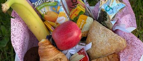 Ein Korb mit einer Banane, einem Apfel, einem Croissant, einem Schokoladenkeks und mehreren Capri-Suns.