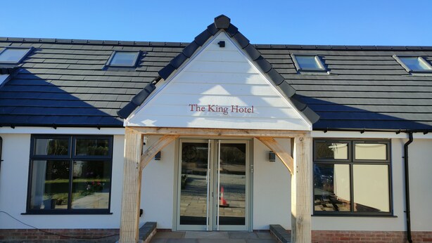 Ein Hotel Eingang mit einem Schild, auf dem 'The King Hotel' steht, mit einem Satteldach, großen Fenstern und einem Backsteinfundament.