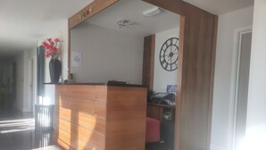 Ein Empfangsbereich mit einem Holzbüro, einer Uhr und einer Vase mit roten Blumen.