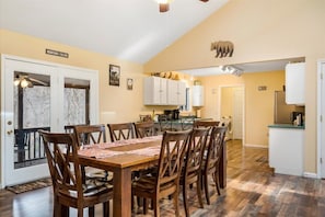 A dining area with a wooden table and chairs, a kitchen with white cabinets, and a sign reading "Mountains are Calling".