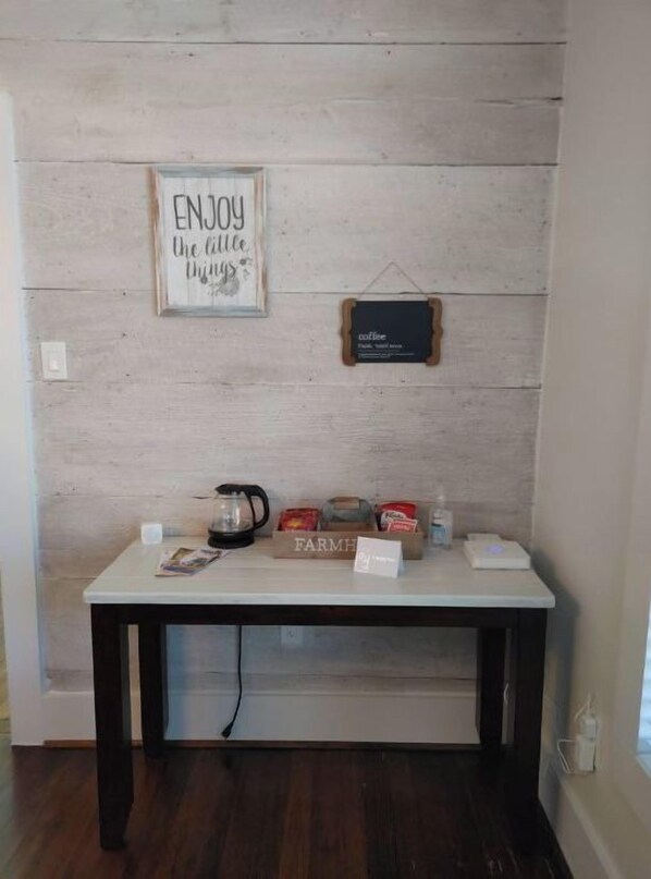 A small table with a coffee maker, a jar, and a box labeled "FARM" against a wooden wall.