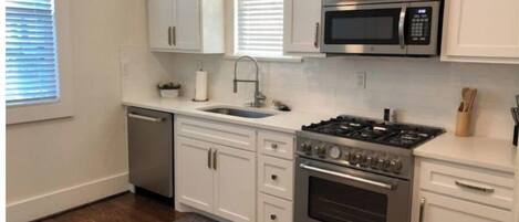 A modern kitchen with white cabinets, a stainless steel stove, a microwave, and a dishwasher.