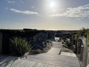 A wooden deck leading to a sandy area with a fence and greenery. - Superb apartment with garden "feet in the water". (La Turballe)