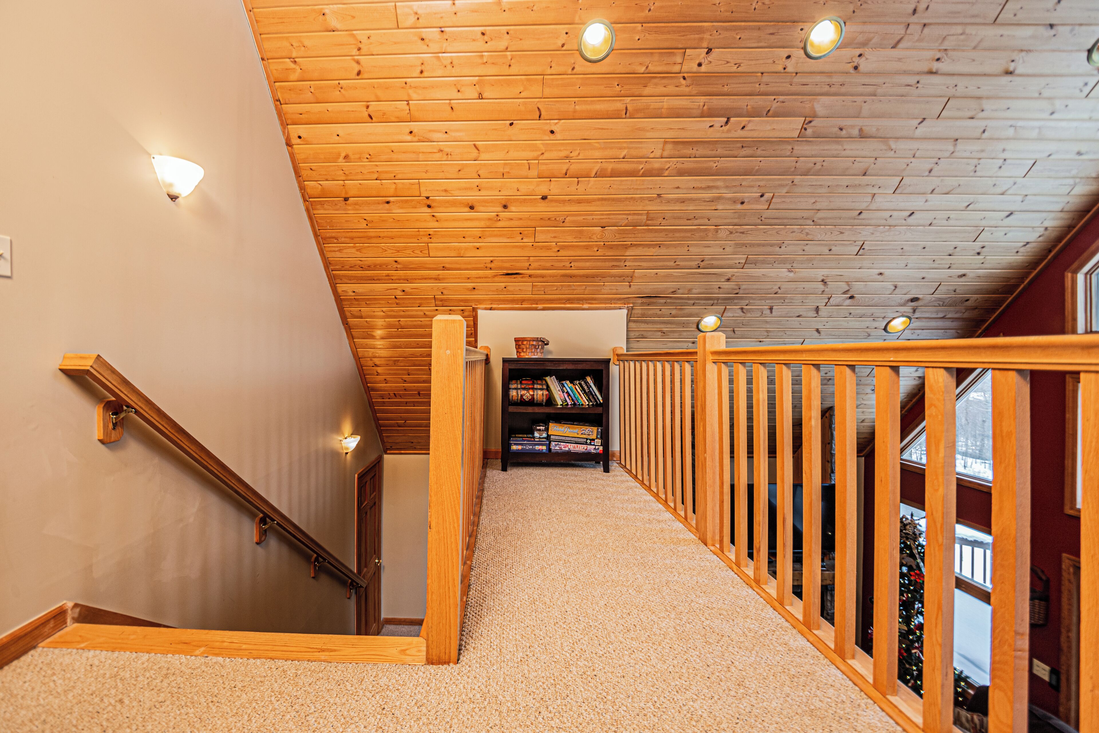 A wooden staircase with a railing, carpeted steps, and a bookshelf at the top.