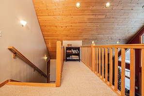 A wooden staircase with a railing, carpeted steps, and a bookshelf at the top.
