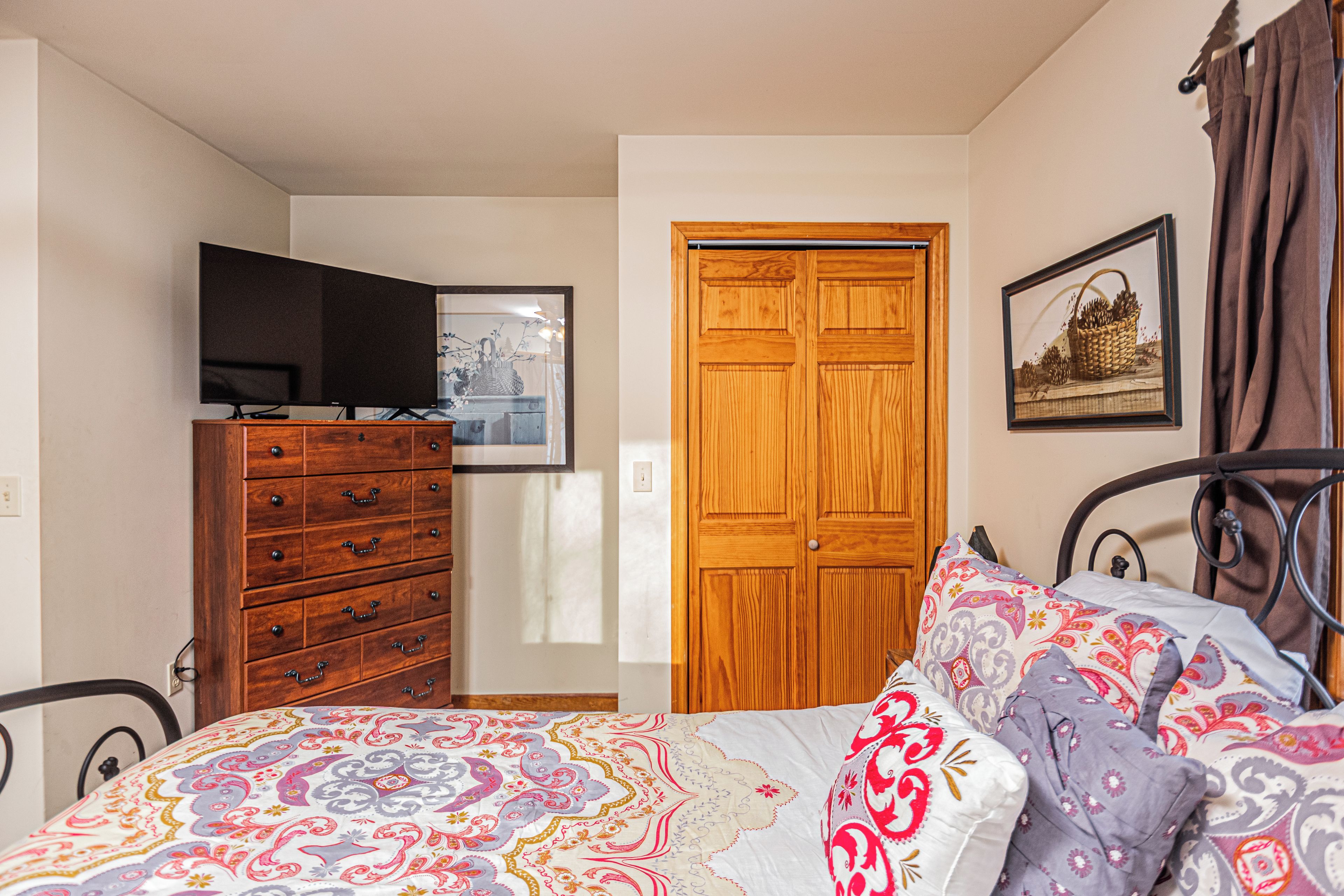 A bedroom with a bed, a dresser, a television, a wooden door, and a framed picture on the wall.