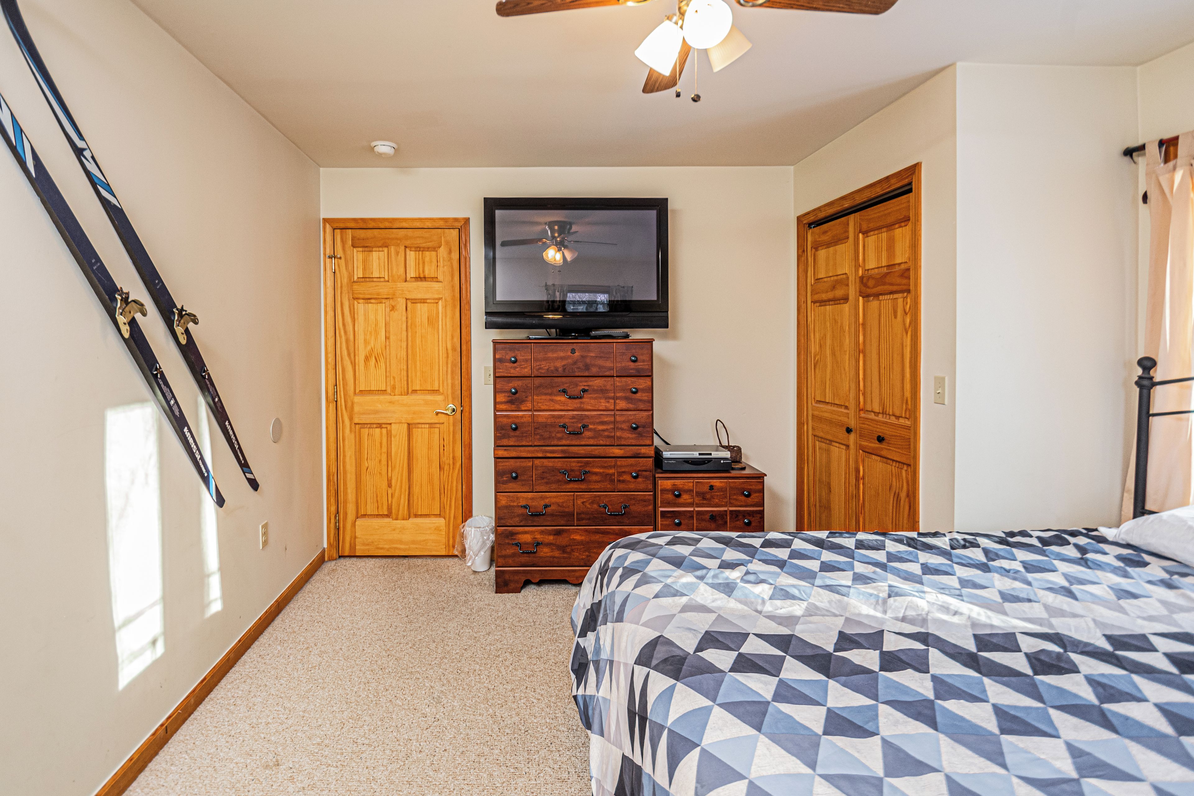 A bedroom with a bed, a dresser, a television, and a ceiling fan.