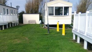 A grassy backyard with a white mobile home, a white fence, and a street lamp. - Charming 3-bed Caravan in Camber Food Rest (Rye)