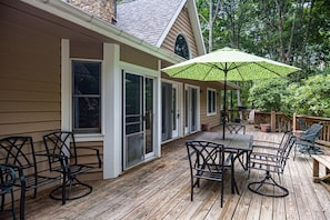 A wooden deck with outdoor furniture, a covered patio area, and a view of a house with large windows and a deck railing.