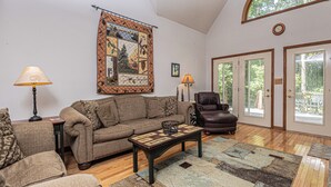 A living room with a sofa, armchair, coffee table, and a large quilt on the wall. - S'more Fun by Taylor Made Deep Creek (Oakland)