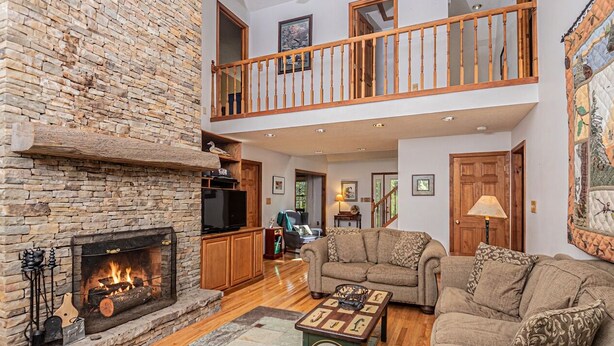 A spacious living area with a stone fireplace, a wooden balcony, and a cozy seating arrangement. - S'more Fun by Taylor Made Deep Creek (Oakland)
