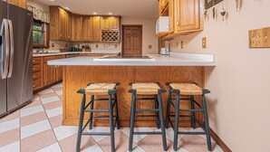 A kitchen with wooden cabinets, a large island with stools, a refrigerator, and various kitchen appliances. - S'more Fun by Taylor Made Deep Creek (Oakland)