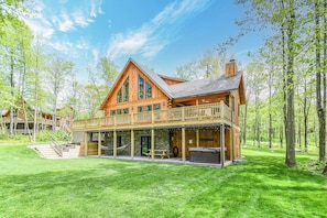 A large wooden cabin with a balcony, a stone foundation, and a grassy yard.