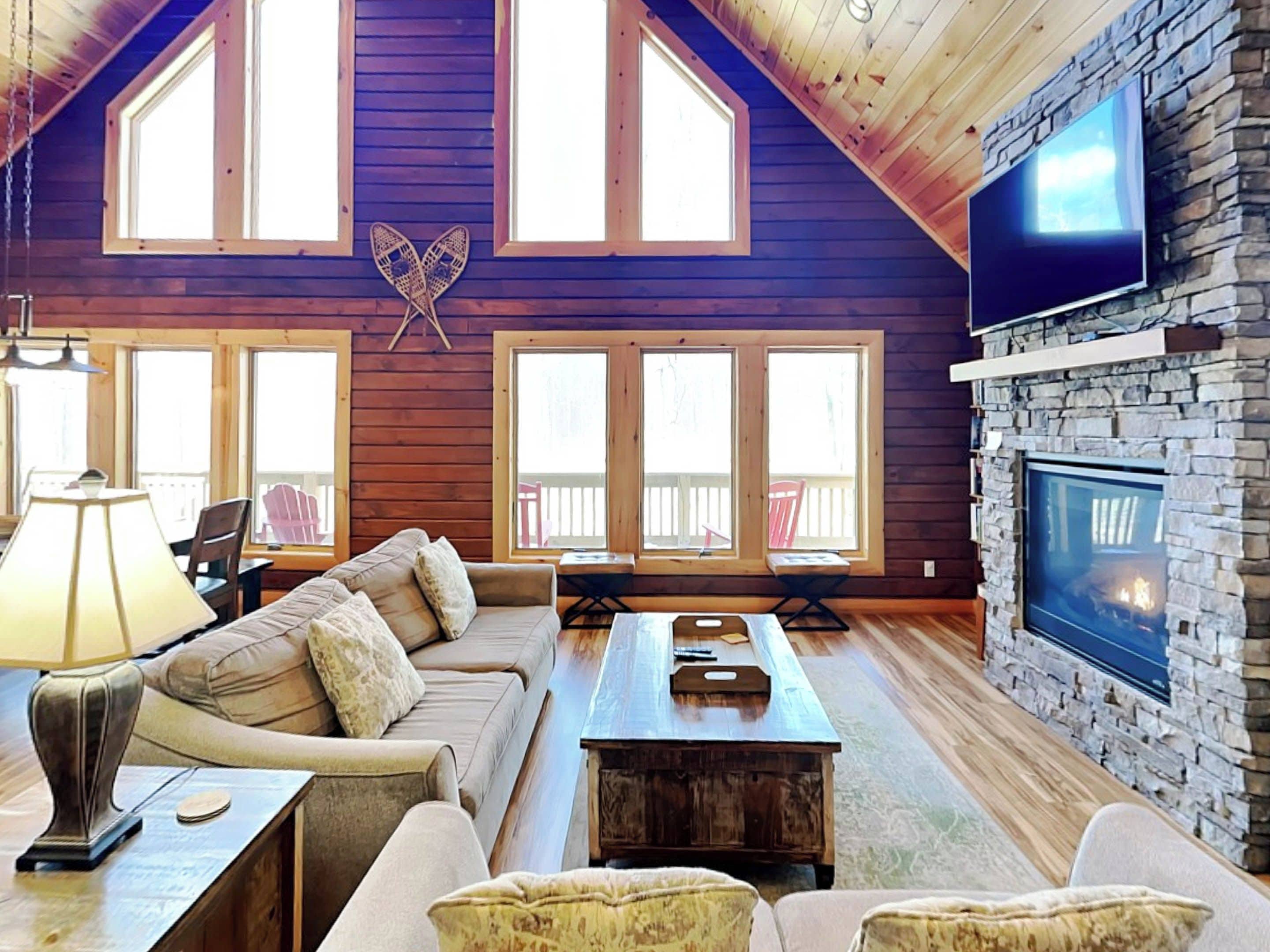 Una sala acogedora con chimenea de piedra, techo de madera y ventanas grandes.