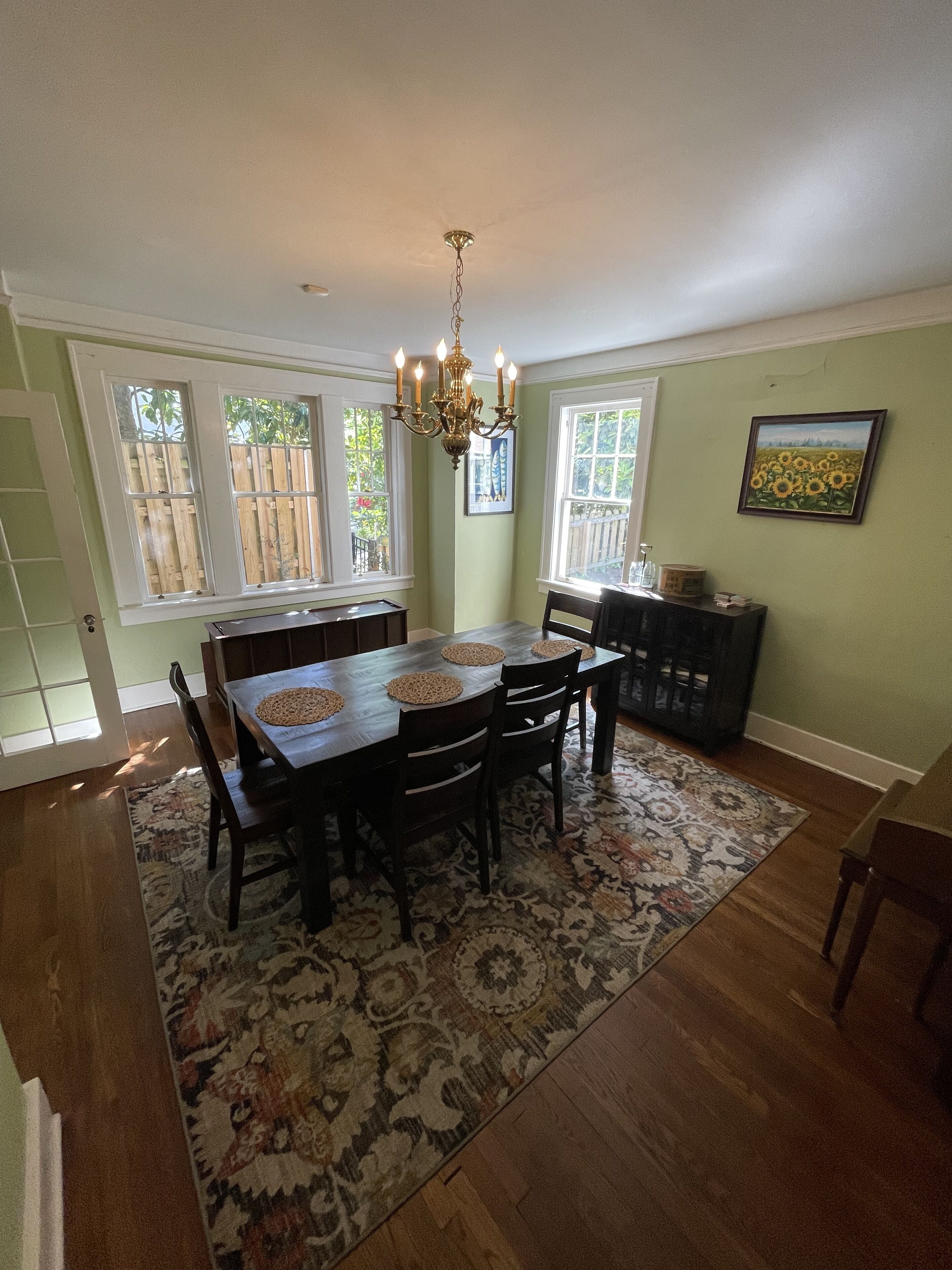 A dining area with a wooden table, chairs, a patterned rug, and a chandelier.