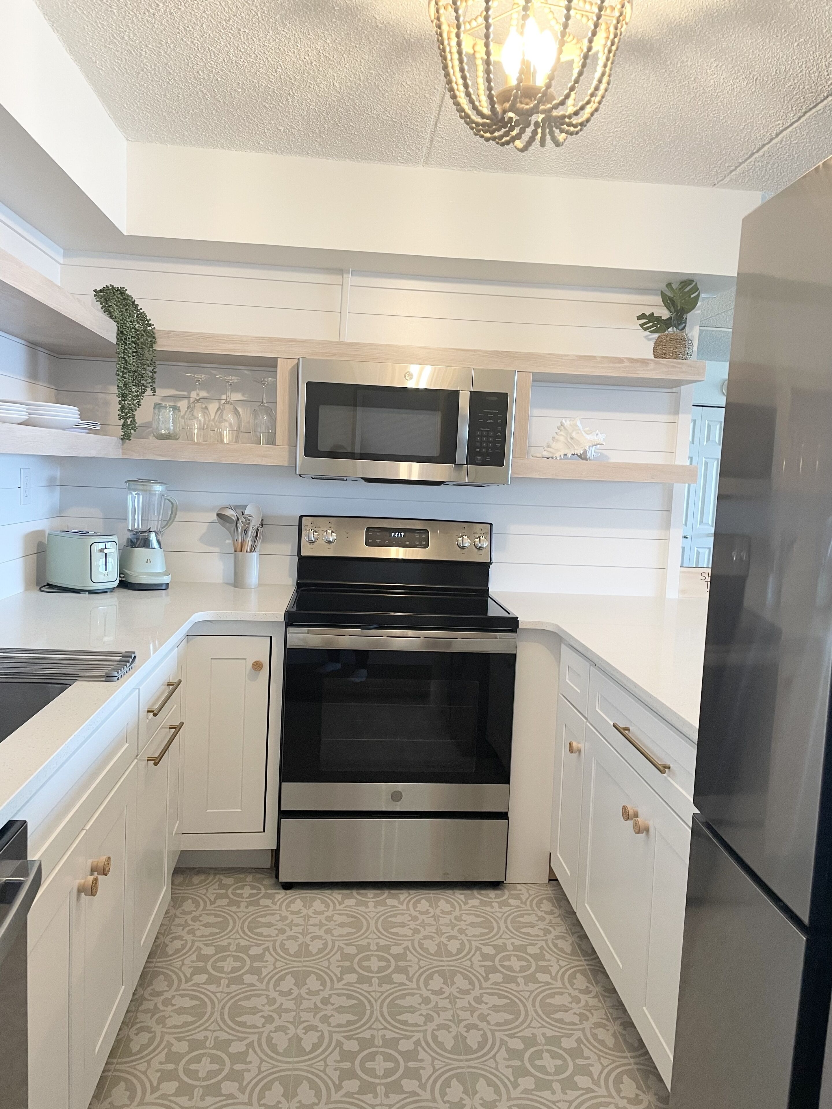 Una cocina moderna con armarios blancos, un refrigerador de acero inoxidable, un microondas, un horno y una araña.