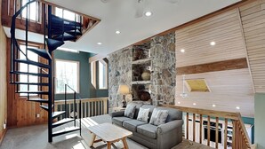 A modern interior with a spiral staircase, a stone accent wall, a grey sofa, and a wooden coffee table.