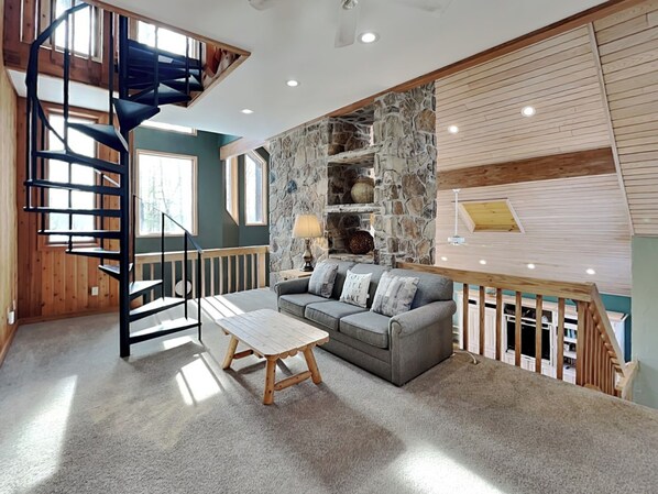 A modern interior with a spiral staircase, a stone accent wall, a grey sofa, and a wooden coffee table.