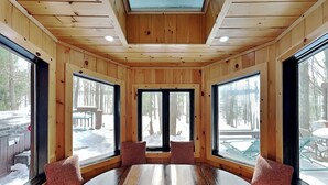 A wooden interior with a round table, large windows, and a view of a snowy outdoor area.