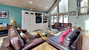 A spacious living room with leather sofas, a glass coffee table, wooden cabinets, and large windows.