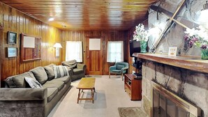 Ein gemütliches Zimmer mit Holzboden, einer Couch, einem kleinen Tisch, einem Stuhl, einem Kamin und einer Steinwand.