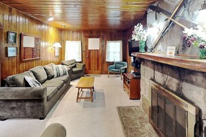 Una habitación acogedora con techo de madera, un sofá, una mesita, una silla, una chimenea y una pared de piedra.