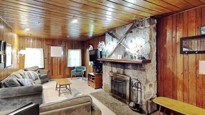 Ein gemütliches Wohnzimmer mit Holzwänden, einem Kamin, einer Couch, einem Couchtisch und einem Fernseher.