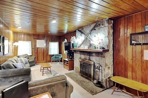 Una sala de estar acogedora con paredes de madera, chimenea, sofá, mesa de centro y televisor.