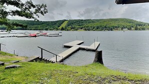 Ein Steg am Seeufer mit einer Treppe zu einer Rasenfläche, umgeben von Hügeln und Booten.