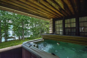 Un jacuzzi con techo de madera y vistas a un lago y árboles.