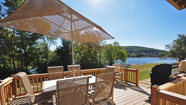 A wooden deck with outdoor furniture, including a table and chairs, and a grill. - Ski Harbor 07 by Taylor Made Deep Creek (McHenry)