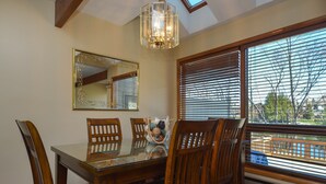 A dining room with a glass table, wooden chairs, a chandelier, a large mirror, and a view through window blinds. - Ski Harbor 07 by Taylor Made Deep Creek (McHenry)