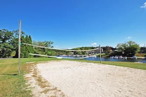 A sandy beach area with a volleyball net, a grassy field, and a lake with boats in the background. - Ski Harbor 07 by Taylor Made Deep Creek (McHenry)