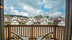 A wooden deck with two white plastic chairs, overlooking a row of townhouses with attached garages and a hilly landscape in the background.