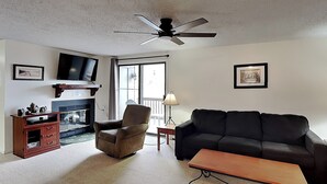 A living room with a sofa, armchair, coffee table, TV, fireplace, and ceiling fan.