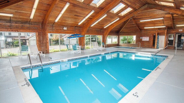 An indoor swimming pool with wooden beams, clear glass walls, and a blue pool.