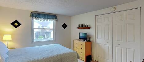 A bedroom with a bed, dresser, TV, and closet.