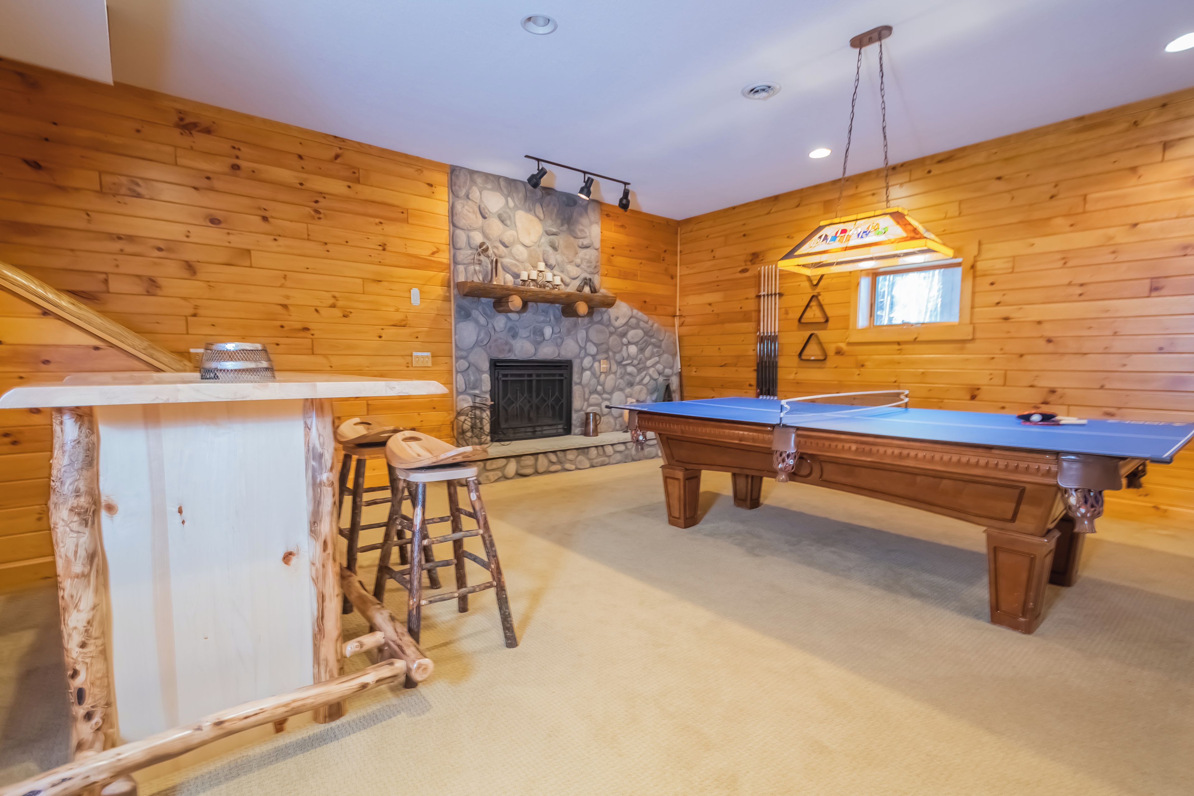 A cozy room with a pool table, a bar area, and a stone fireplace.