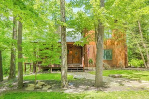 A rustic log cabin with a stone pathway leading to the entrance, surrounded by lush greenery and trees. - Skylodge by Taylor Made Deep Creek (Oakland)