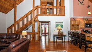 A spacious living area with a wooden staircase, a dining area with wooden chairs and a table, and a kitchen with wooden cabinets. - Slip Away Chalet by Taylor Made Deep Creek (McHenry)