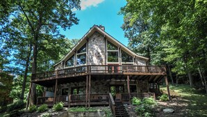 A stone cabin with a wooden balcony, surrounded by trees. - Slip Away Chalet by Taylor Made Deep Creek (McHenry)