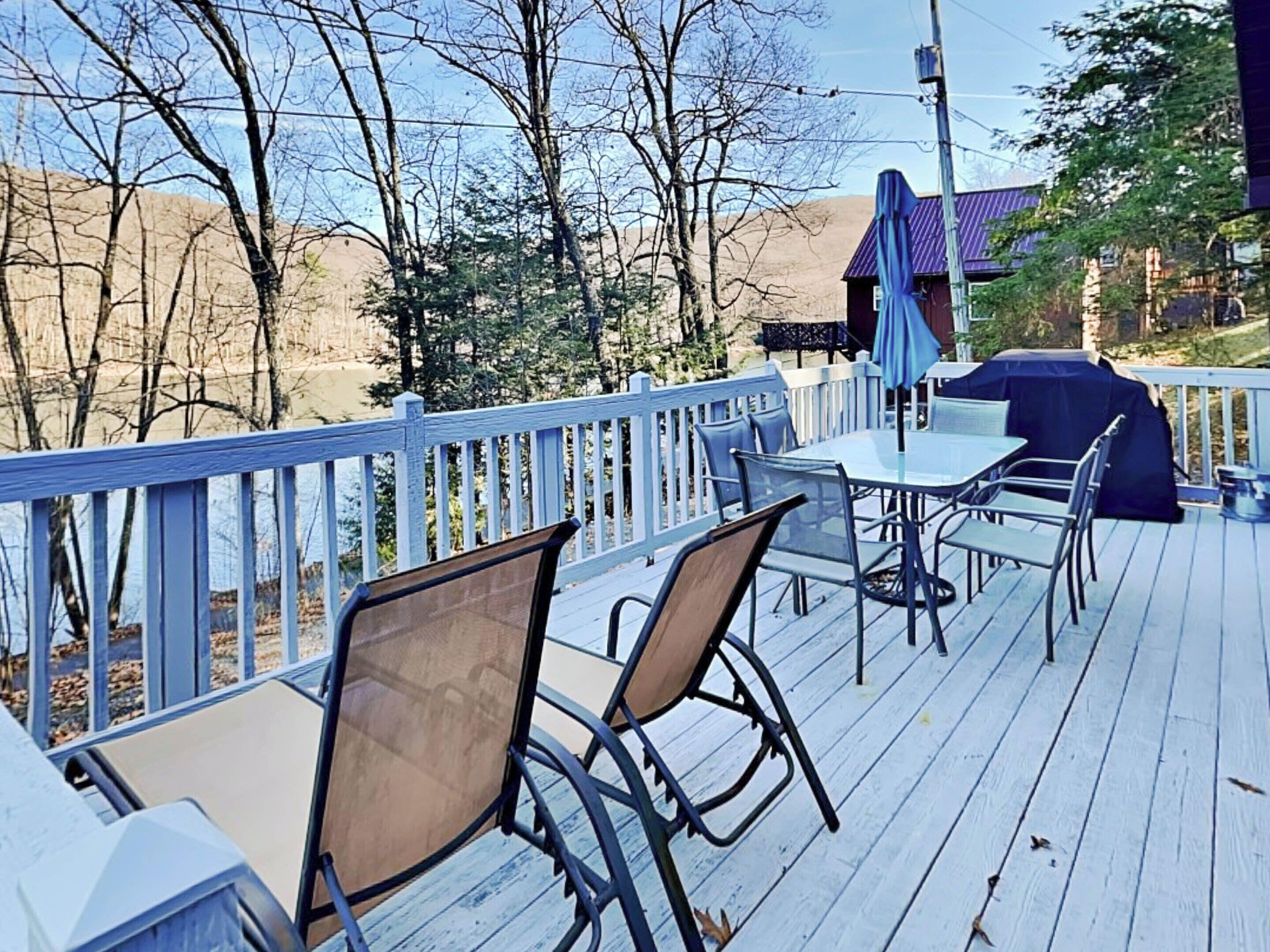 A deck with outdoor seating, a barbecue area, and a view of trees and hills.