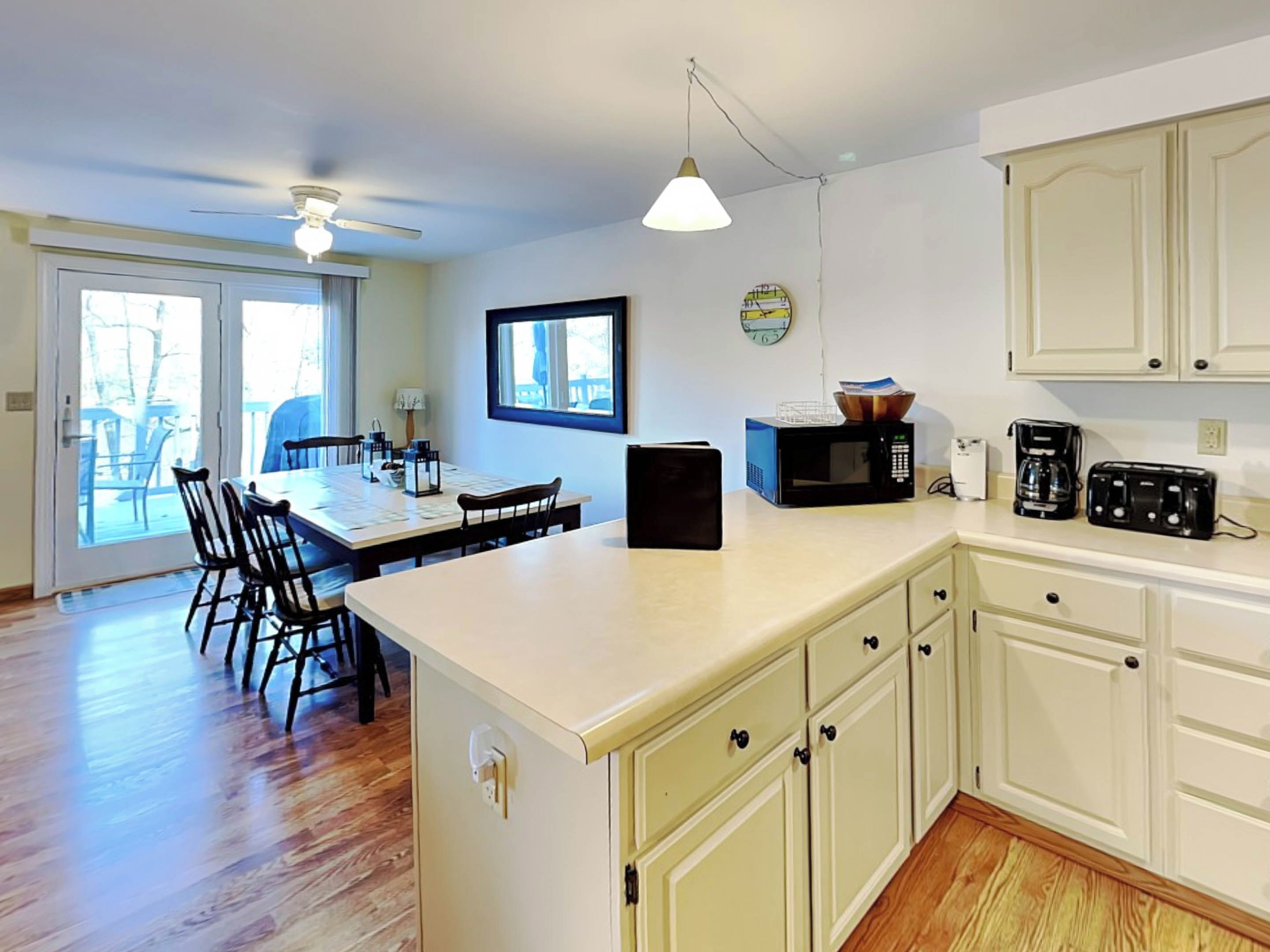 A kitchen with a dining area, white cabinets, a microwave, a toaster, and a clock on the wall.