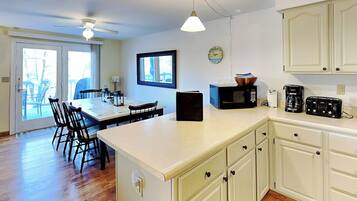 A kitchen with a dining area, white cabinets, a microwave, a toaster, and a clock on the wall.